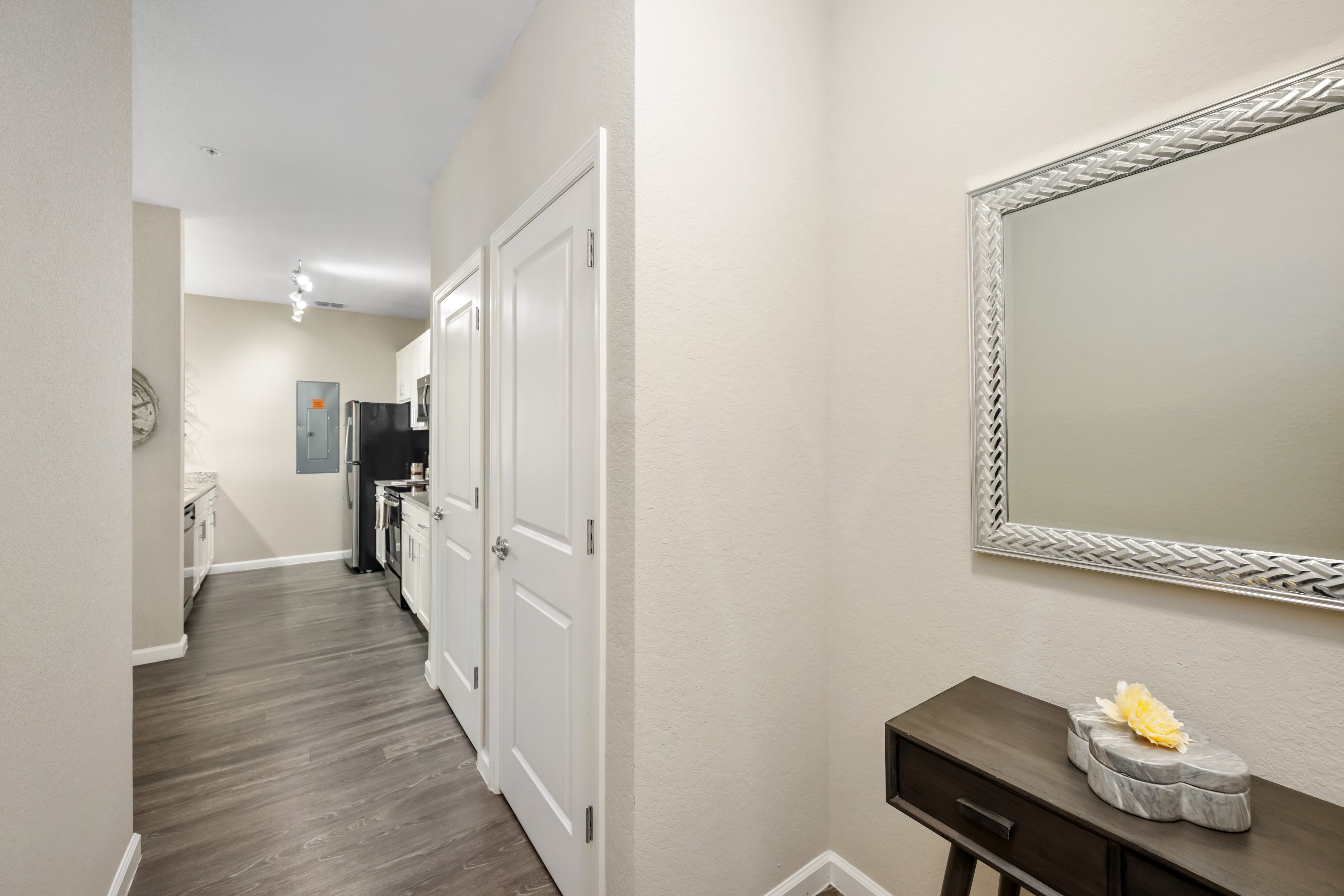 A hallway with a mirror on the wall and a table with a flower on it.